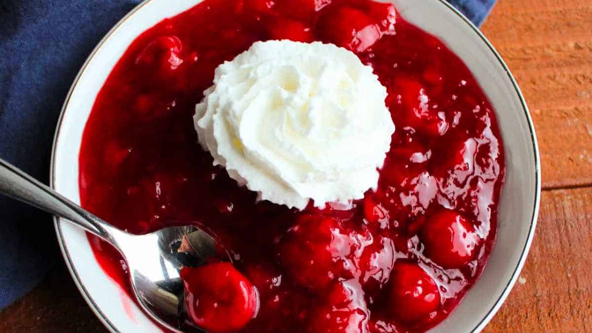 A bowl of cherry sauce with whipped cream and a spoon.
