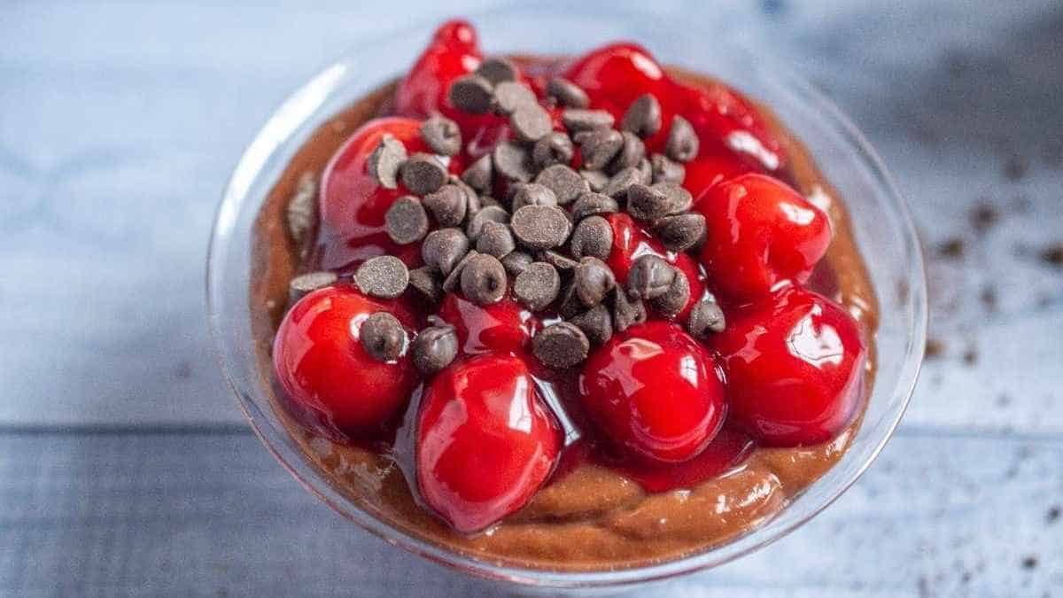 A bowl of chocolate pudding with cherries and chocolate chips.