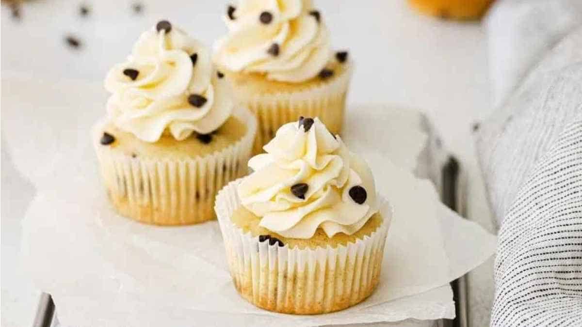 Three cupcakes topped with white frosting and chocolate chips.