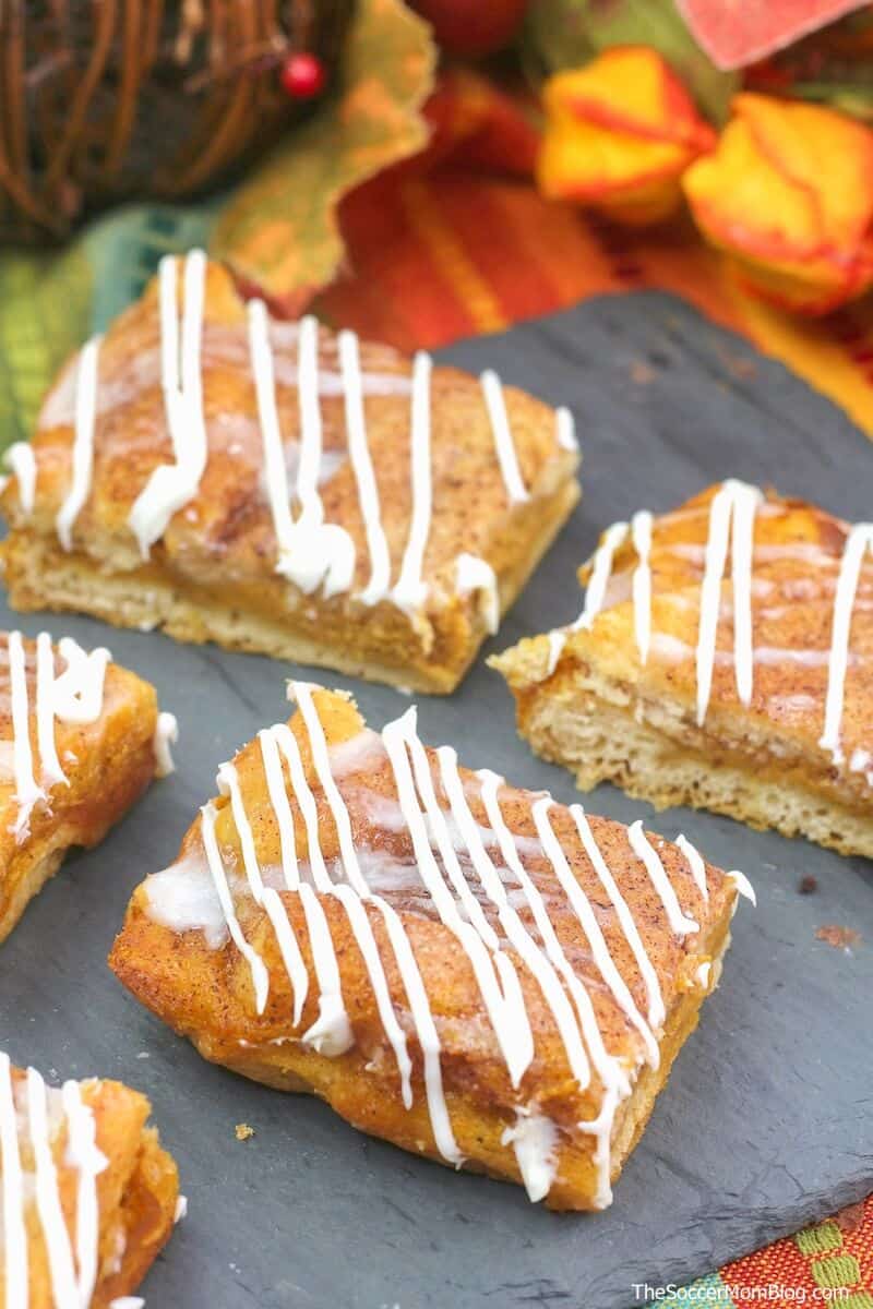 pumpkin cheesecake bars with cream cheese drizzle on a black serving plate.
