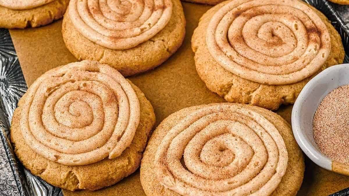 Cinnamon swirl cookies on a baking sheet with a bowl of powdered sugar.