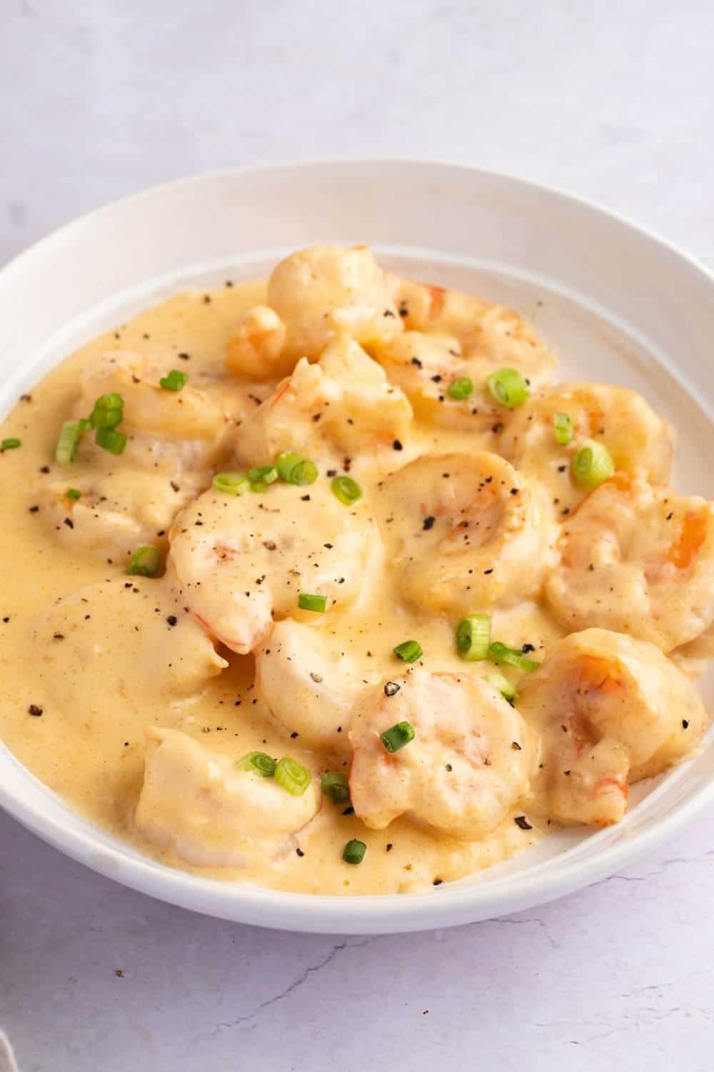 Creamy Shrimp Newburg in a White Bowl, Garnished With Sliced Onions and Black Pepper.
