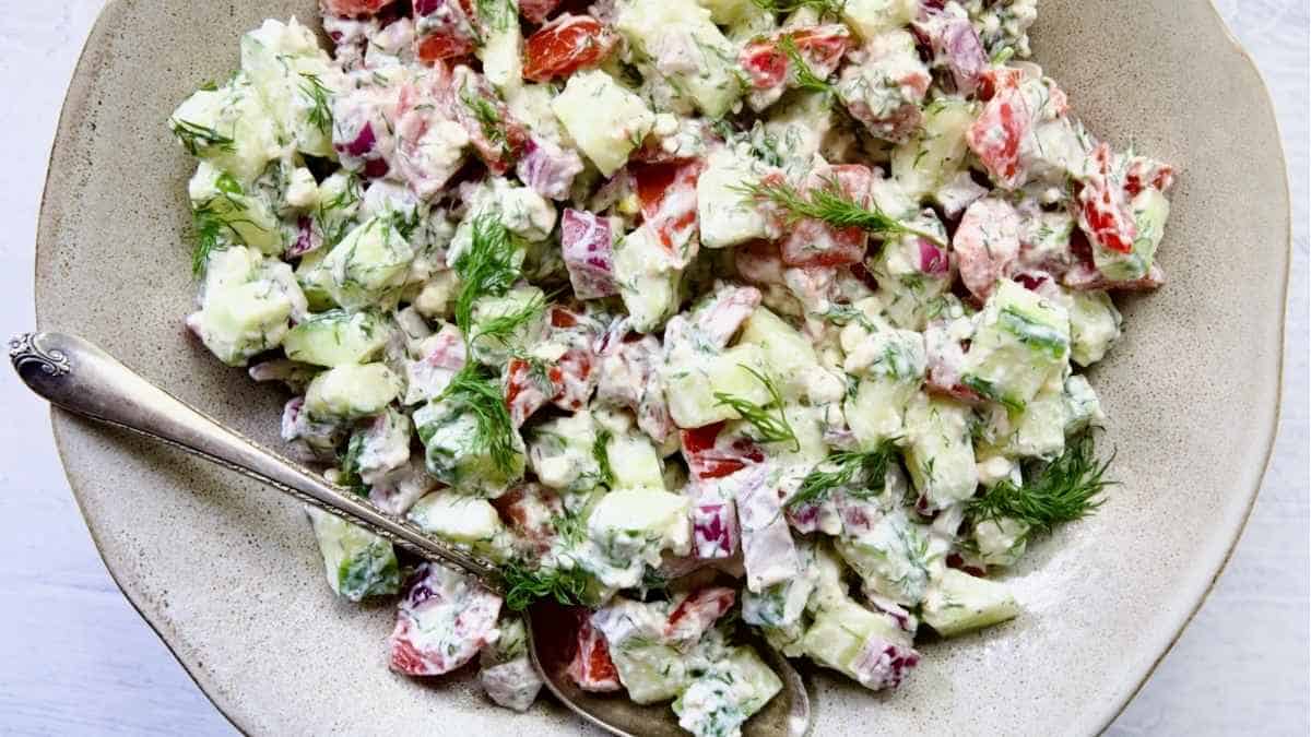 A bowl of cucumber salad with tomatoes and dill.