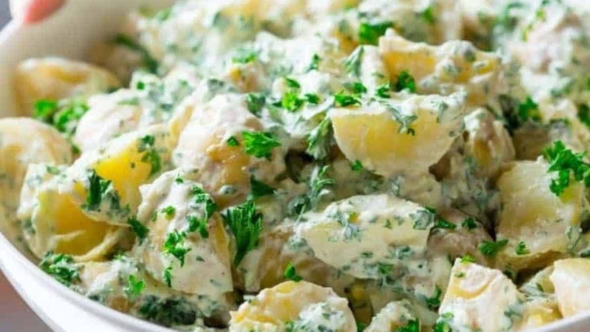 A person holding a bowl of potato salad with parsley.