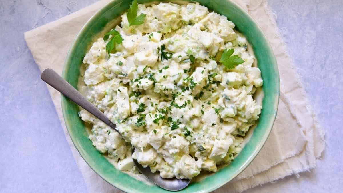 A green bowl of potato salad with a spoon.