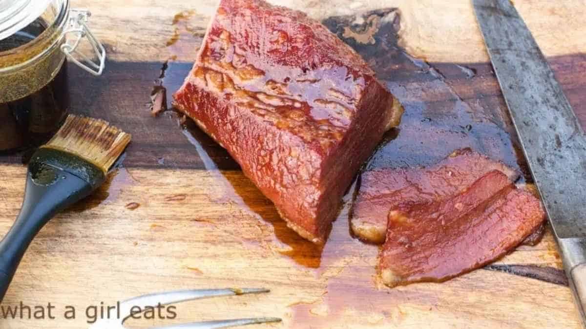 A piece of beef is sitting on a cutting board with a knife.