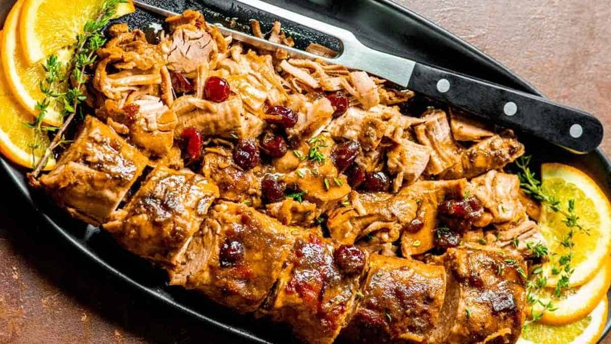 A plate of pulled pork with cranberries and orange slices.