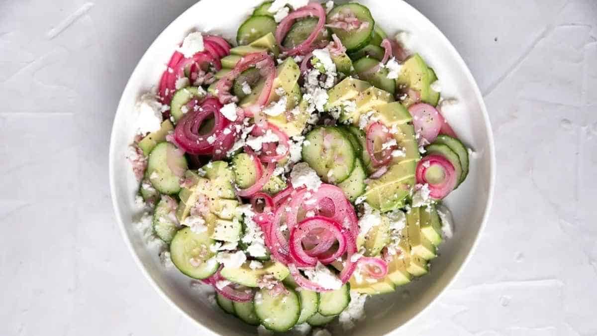 A bowl of cucumber salad with red onions and feta cheese.