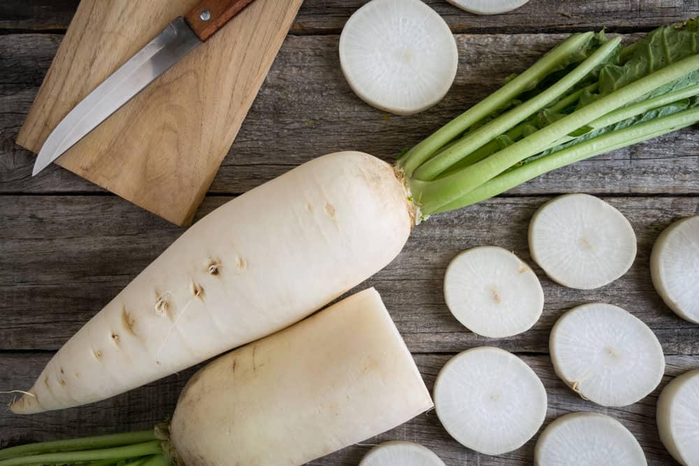 Daikon radishes on a rustic wooden table with a sharp knife.
