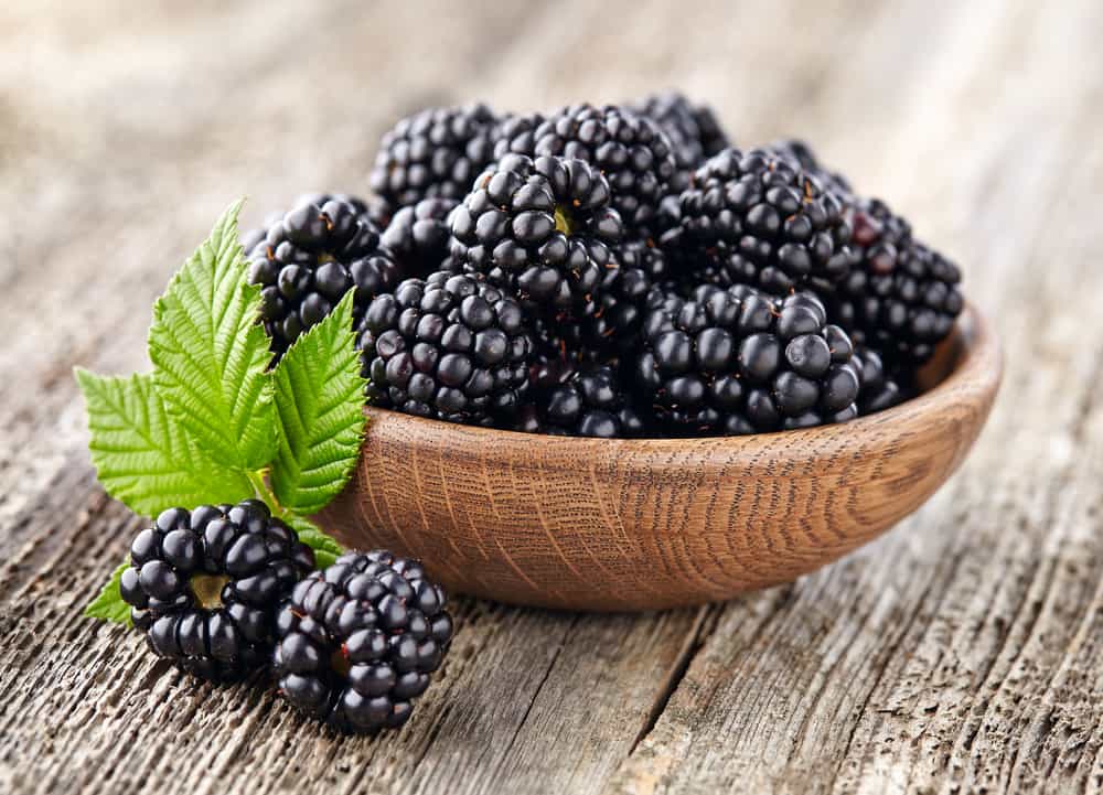 Blackberries in a wooden bowl on a rustic table.