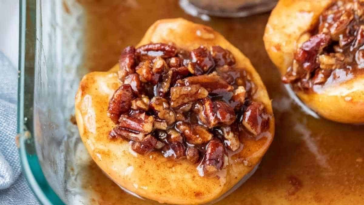 Two apples covered in caramel and pecans in a baking dish.