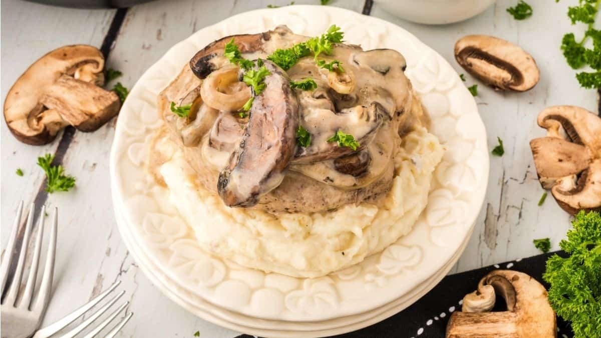 A plate with mushrooms and gravy on top of mashed potatoes.