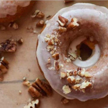 Donuts with icing and pecans on a wooden board.