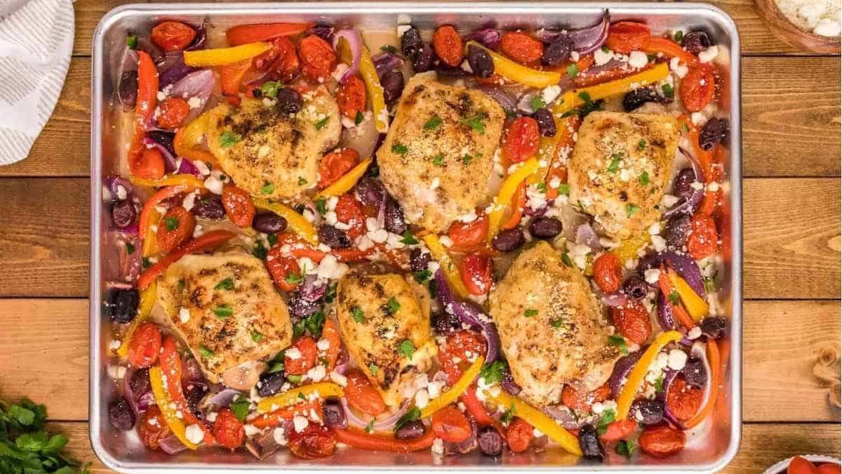 Greek chicken breasts on a baking sheet with vegetables.