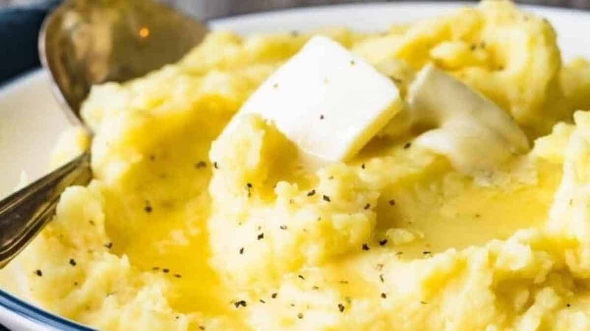 A bowl of mashed potatoes with butter and a spoon.