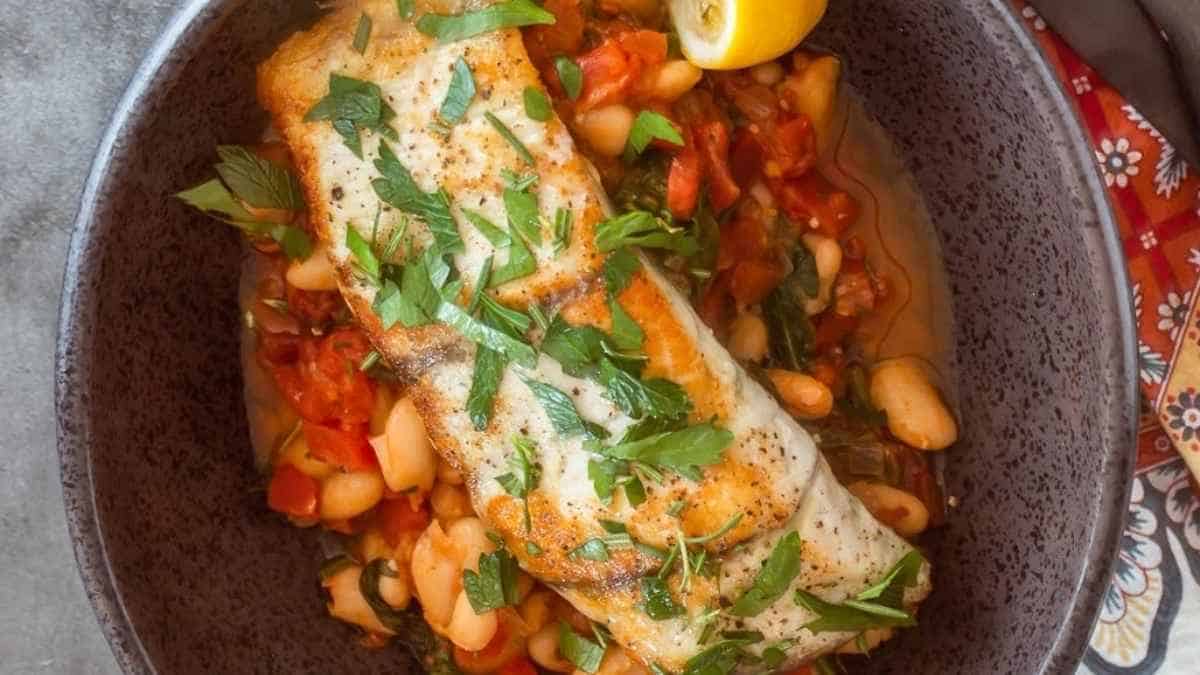 A bowl of fish and beans with a lemon wedge.