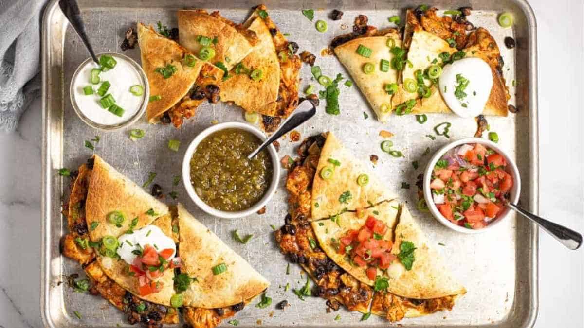 Quesadillas on a baking sheet with dipping sauces.