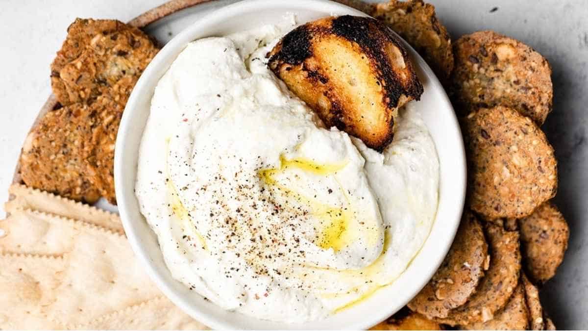 A bowl of hummus with crackers and bread.