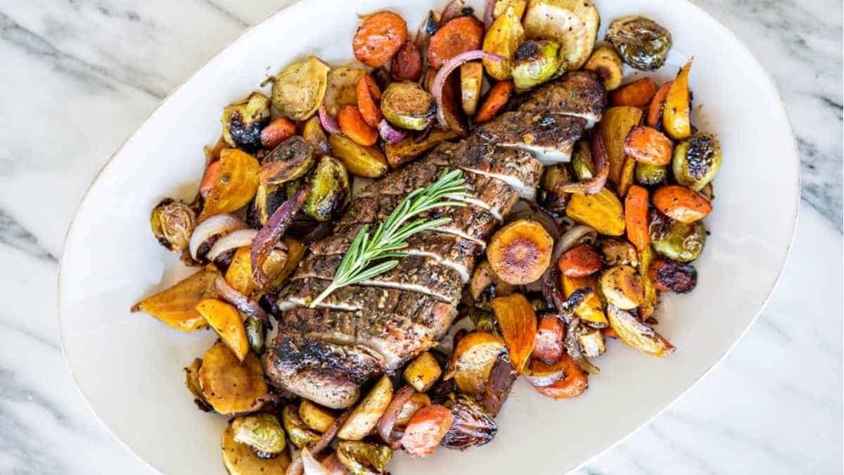 Roasted lamb with roasted vegetables on a white plate.