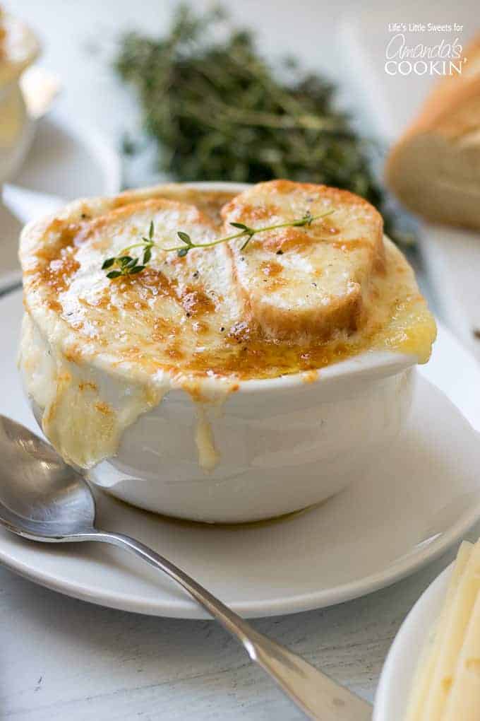 cheesy french onion soup in bowl / Caramelized onions in a reduction of white wine and sherry with herbs of thyme and bay leaves make this French Onion Soup delicious.
