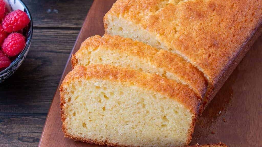 A slice of lemon pound cake on a wooden cutting board.