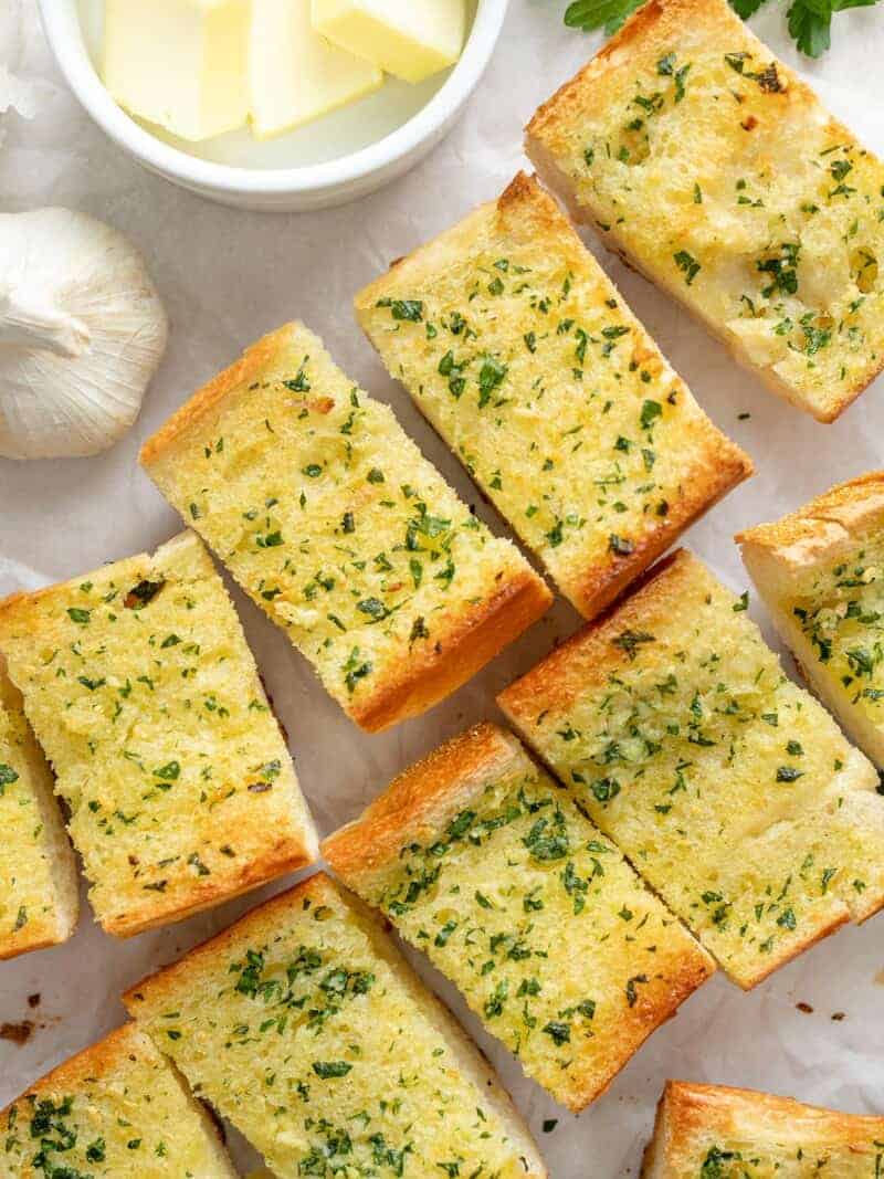 Slices of homemade garlic bread on a surface next to a bowl of butter. / Homemade Garlic Bread is twice as nice for half the price of it's frozen store bought counterpart! An inexpensive and freezer-friendly side dish! 
