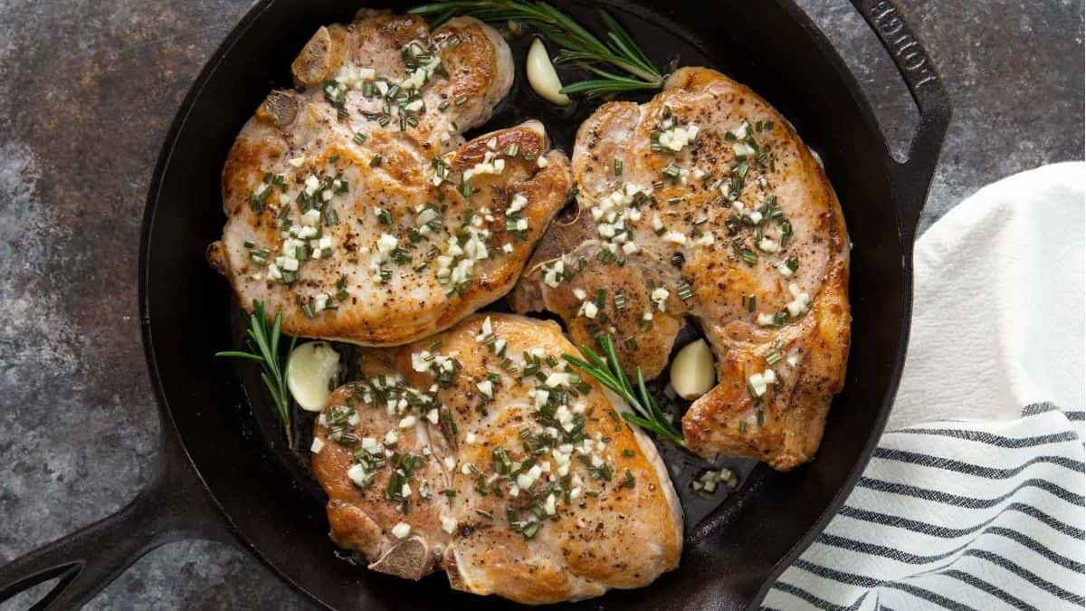 Pork chops in a skillet with herbs and garlic.