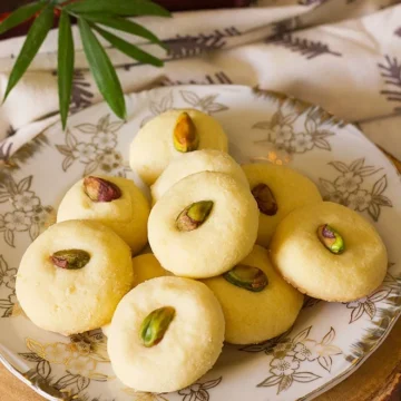 Unique pistachio cookies on a plate with a cup of tea.