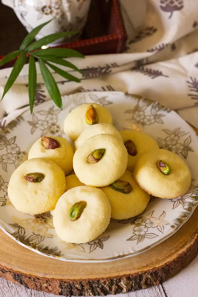 Unique pistachio cookies on a plate with a cup of tea.