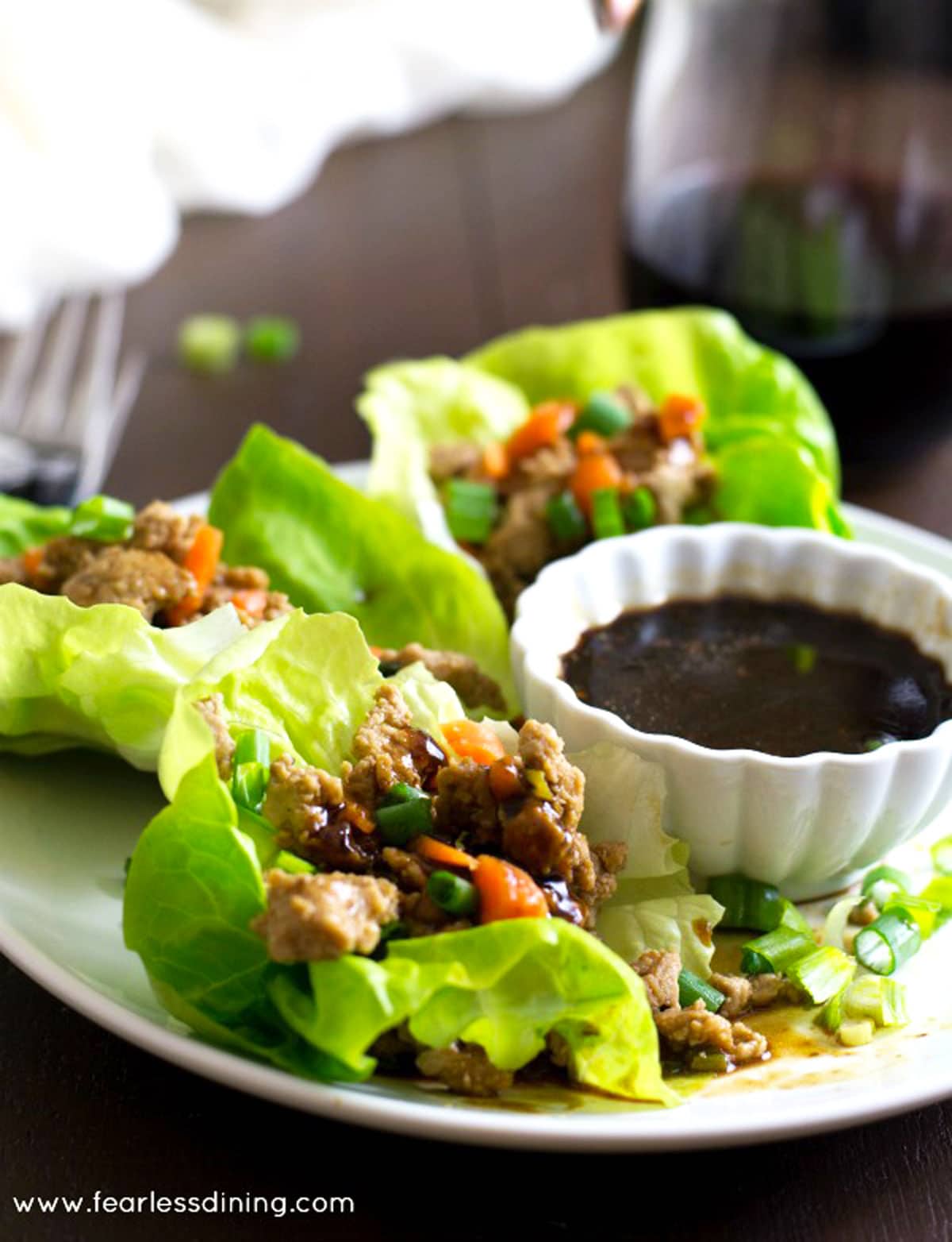 Gluten free lettuce wraps on a plate next to a small bowl of dipping sauce. 
