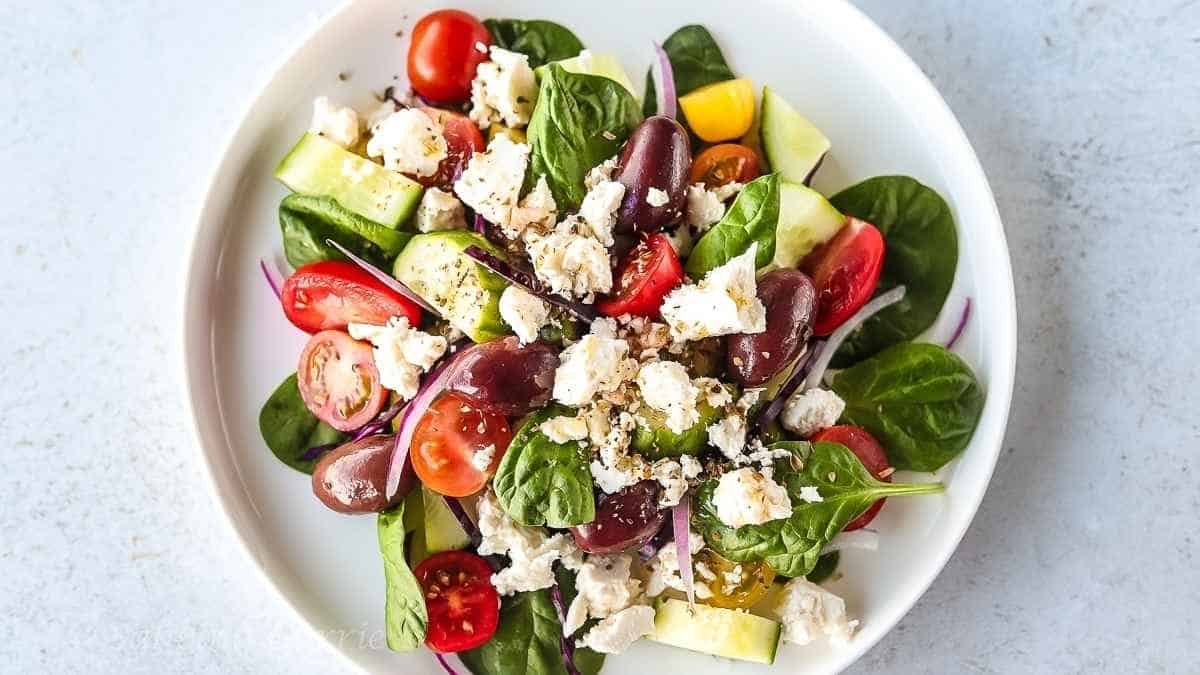 A plate of greek salad with tomatoes, olives and feta cheese.