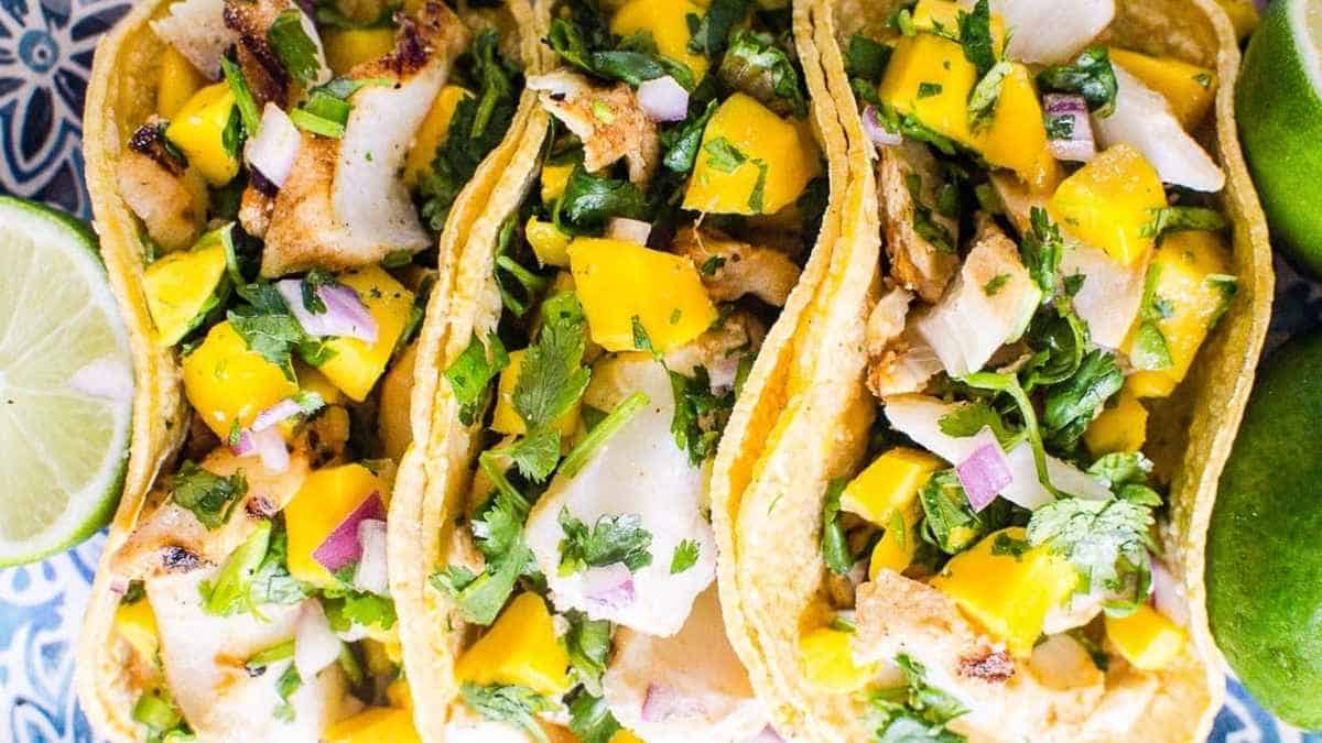Three fish tacos with mango and lime on a blue plate.