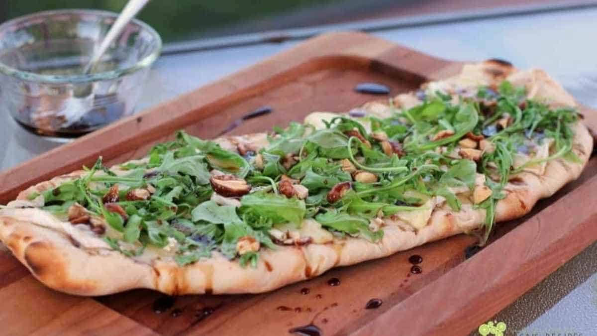 A pizza with arugula and walnuts on a wooden board.