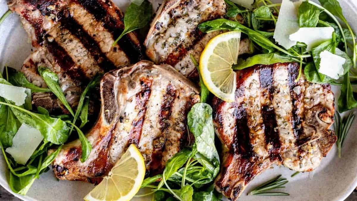 Grilled lamb chops on a plate with lemon wedges and spinach.
