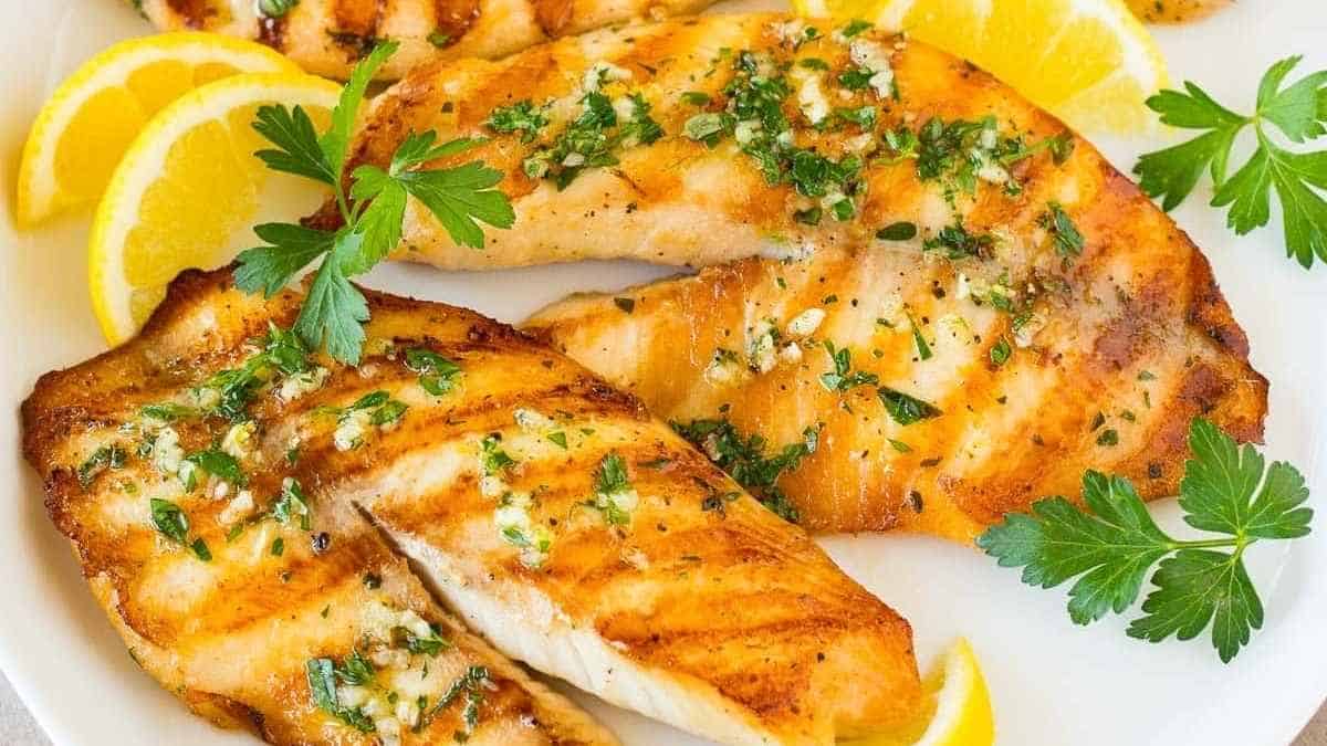 Grilled salmon with lemon slices and parsley on a white plate.