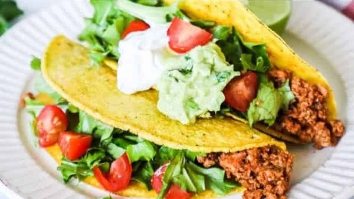 Two tacos on a plate with guacamole and sour cream.