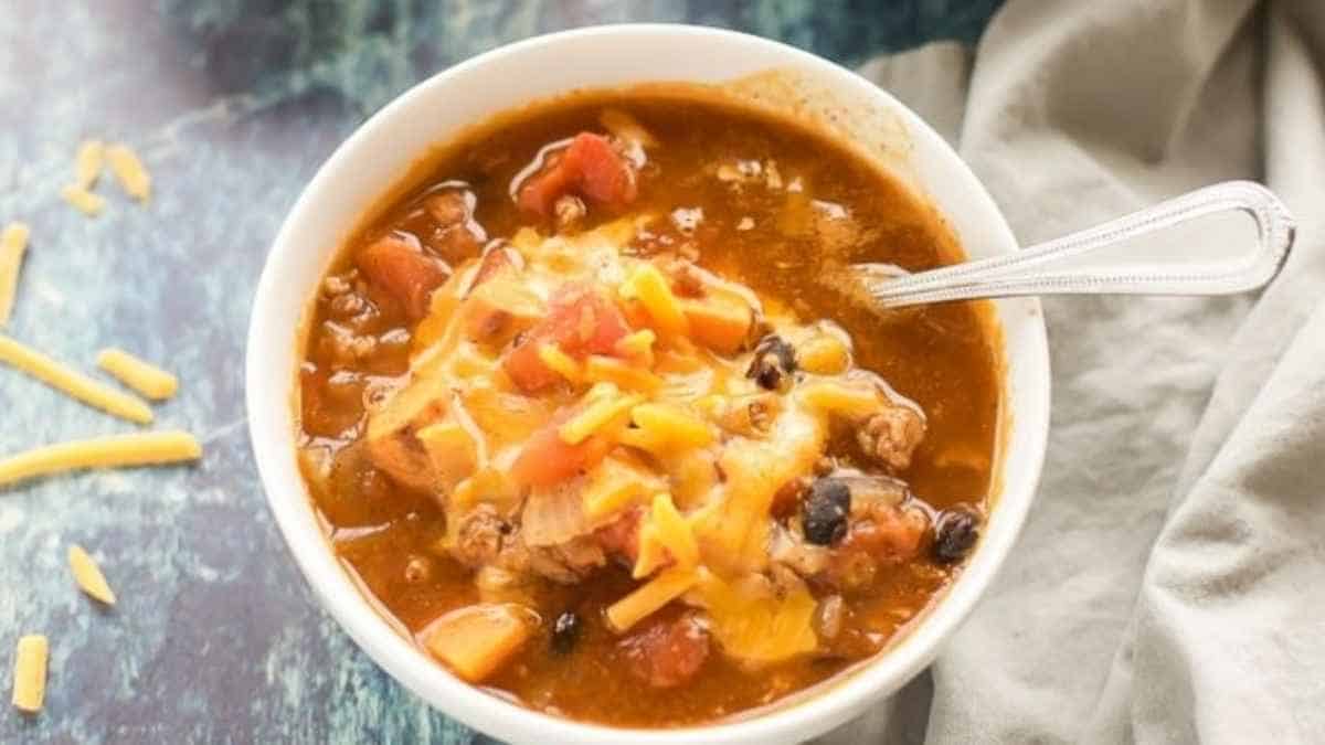 A bowl of mexican chili with cheese in it.