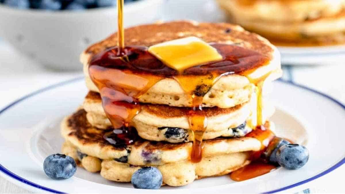 A stack of blueberry pancakes being drizzled with syrup.