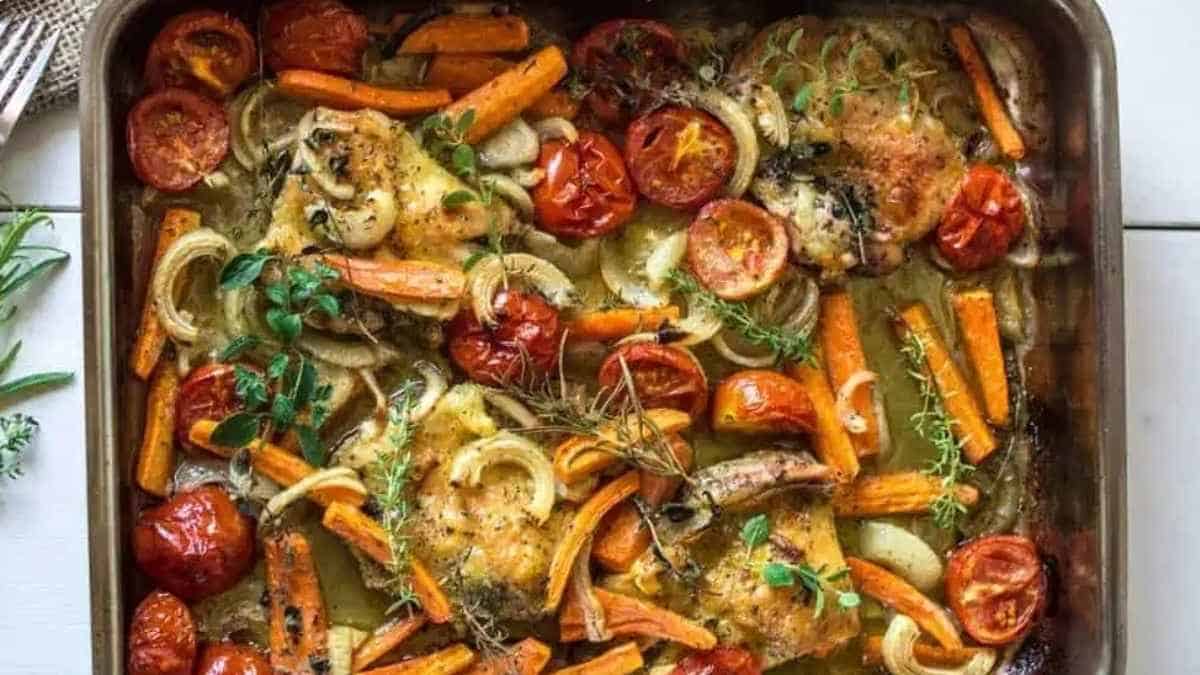 Roasted chicken with tomatoes and thyme on a baking sheet.