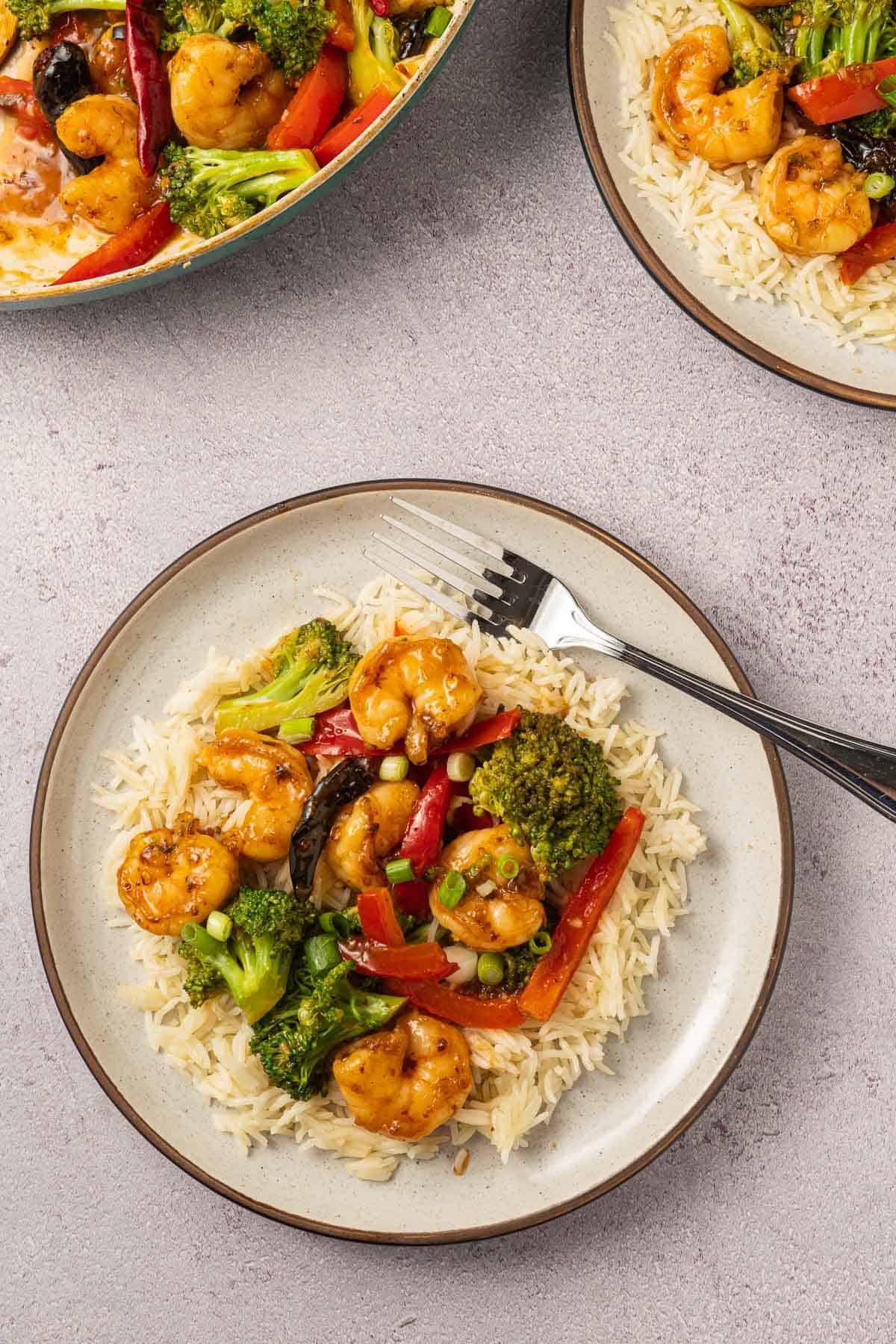 Mongolian shrimp, broccoli, red pepper, chili pepper with cauliflower rice on beige plate and fork. 
