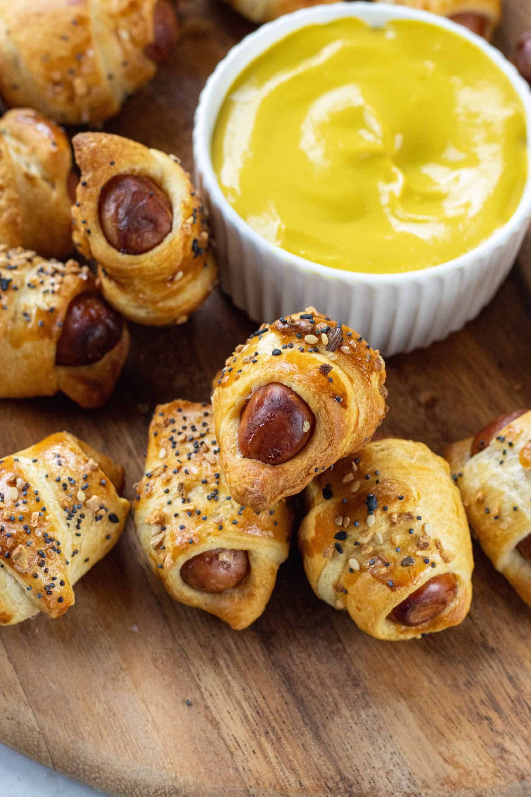 Pigs in a Blanket on a wooden plate with mustard.
