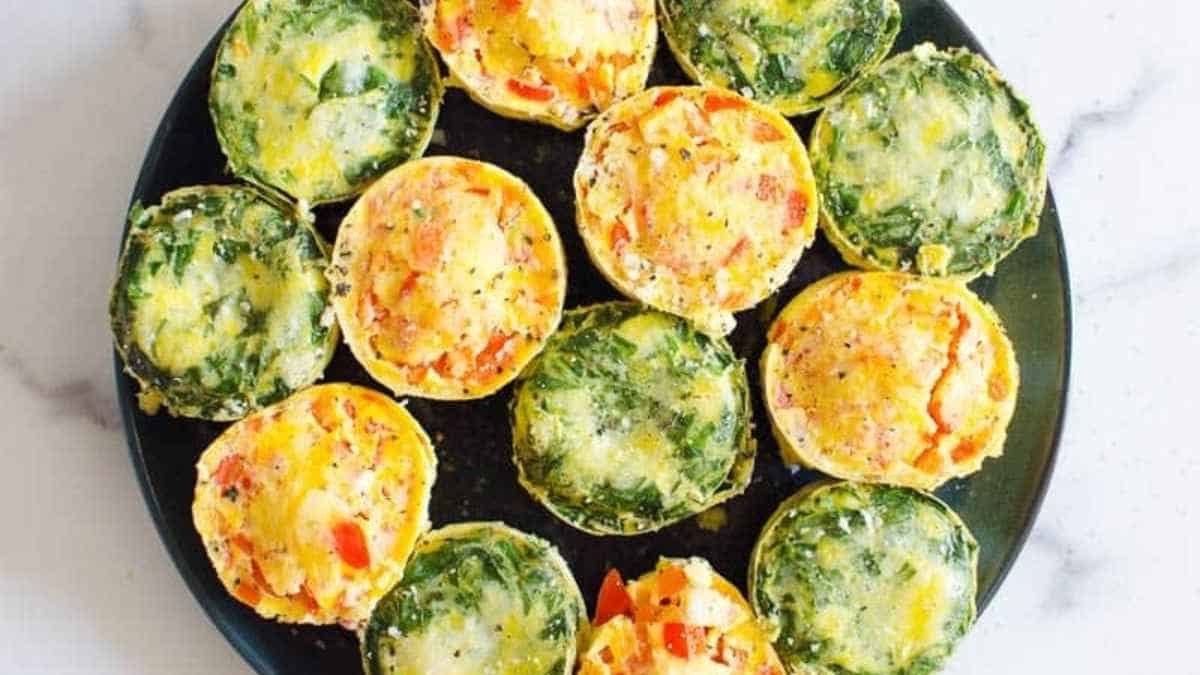 A plate of spinach and egg muffins on a marble counter.