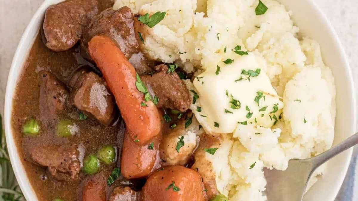 A bowl of beef stew with carrots and mashed potatoes.
