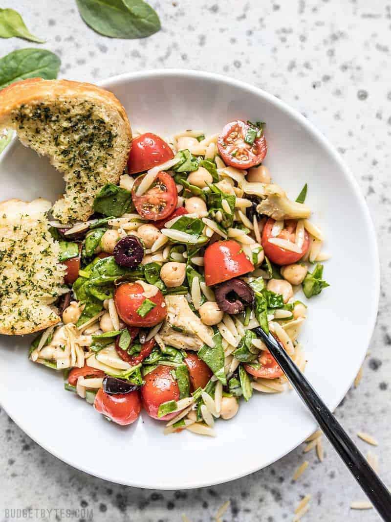 Italian Orzo Salad on a plate with a piece of garlic bread on the side. / Filling enough to serve as a light meal, but light enough to act as an easy side dish, this Italian Orzo Salad is a versatile addition to your weekly meal prep. 
