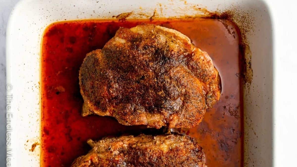 Two pork chops in a baking dish with sauce.
