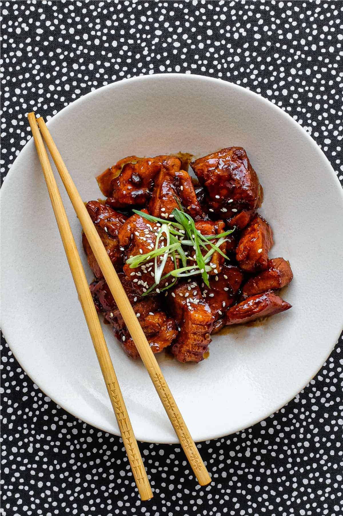 A white plate with chicken and chopsticks on it, showcasing delicious pork belly recipes.
