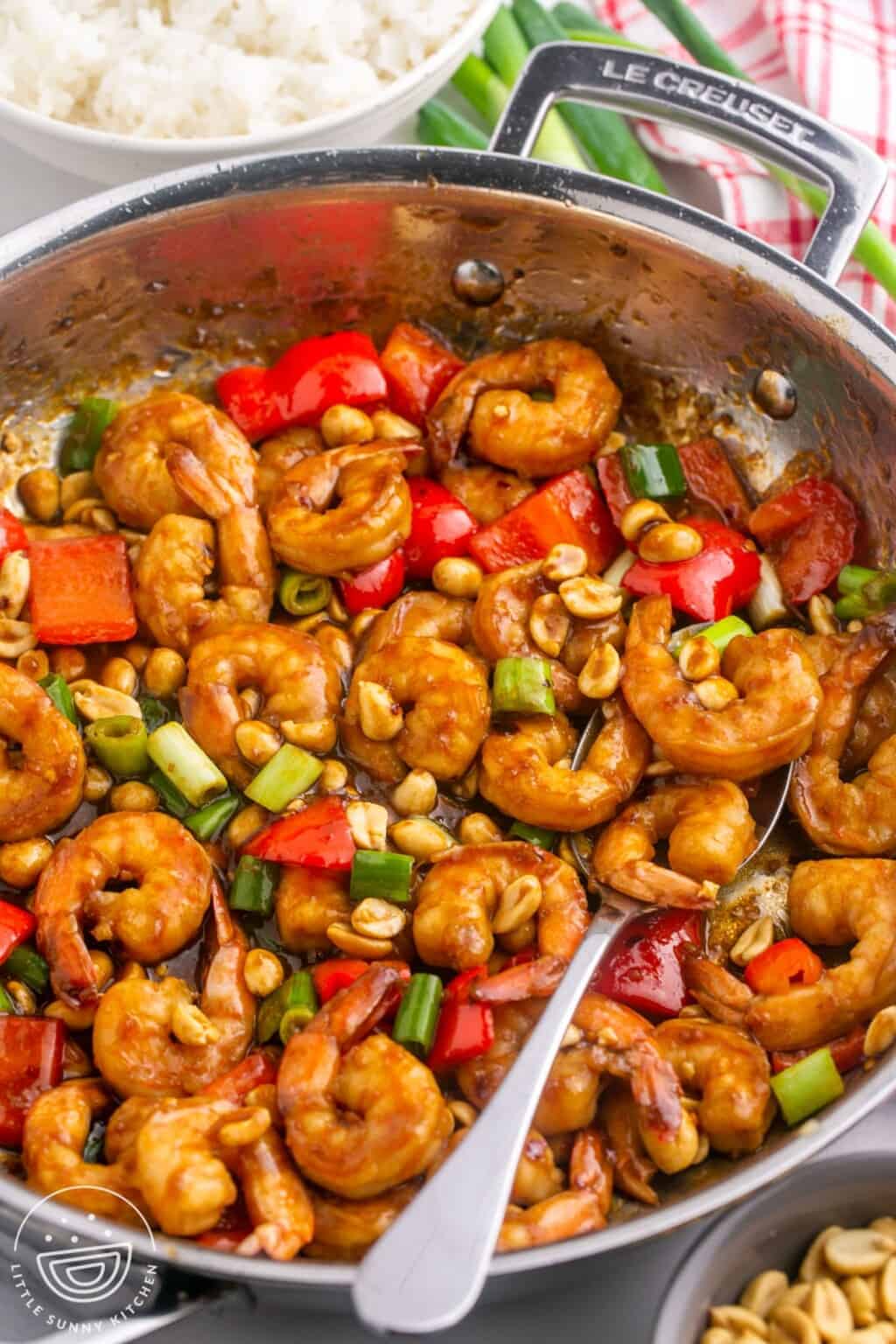 Kung pao shrimp in a skillet with a serving spoon.
