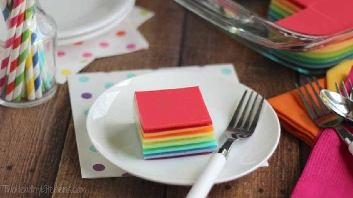 Rainbow cake on a plate with a fork and spoon.