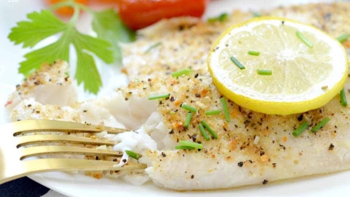 Fish fillet with lemon and parsley on a white plate.