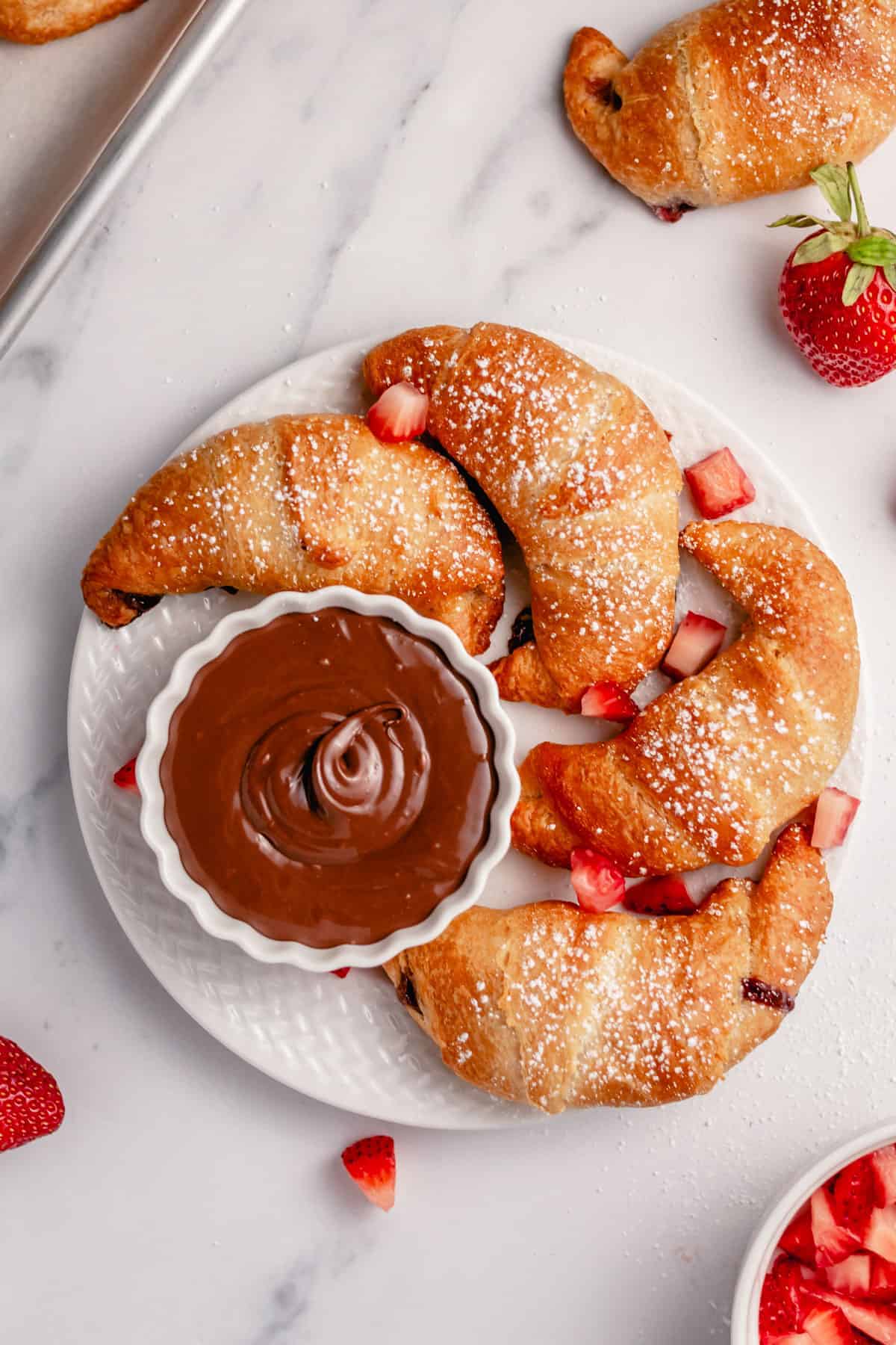 nutella crescent rolls surrounded by strawberry slices on a white serving plate.
